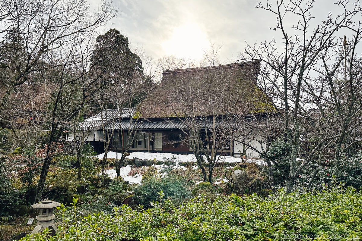 traditional Japanese house with thatched roof in back of a garden