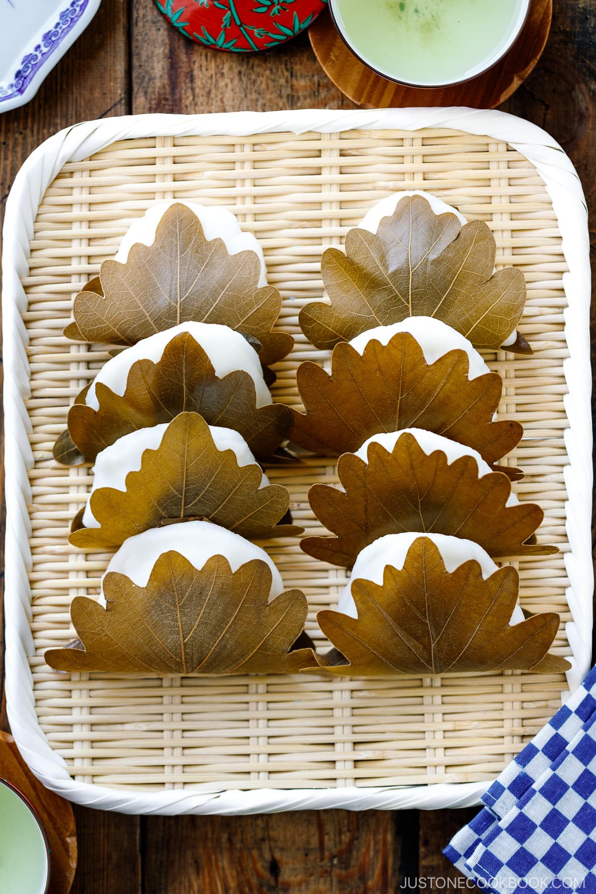 A rectangular bamboo basket containing eight pieces of Kashiwa Mochi, a Japanese sweet red bean filled mochi wrapped in oak leaf.