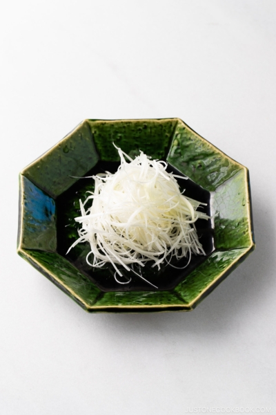 A green plate containing Shiraga Negi (Julienned Long Green Onion Garnish).