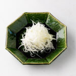 A green plate containing Shiraga Negi (Julienned Long Green Onion Garnish).