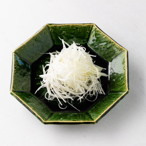 A green plate containing Shiraga Negi (Julienned Long Green Onion Garnish).