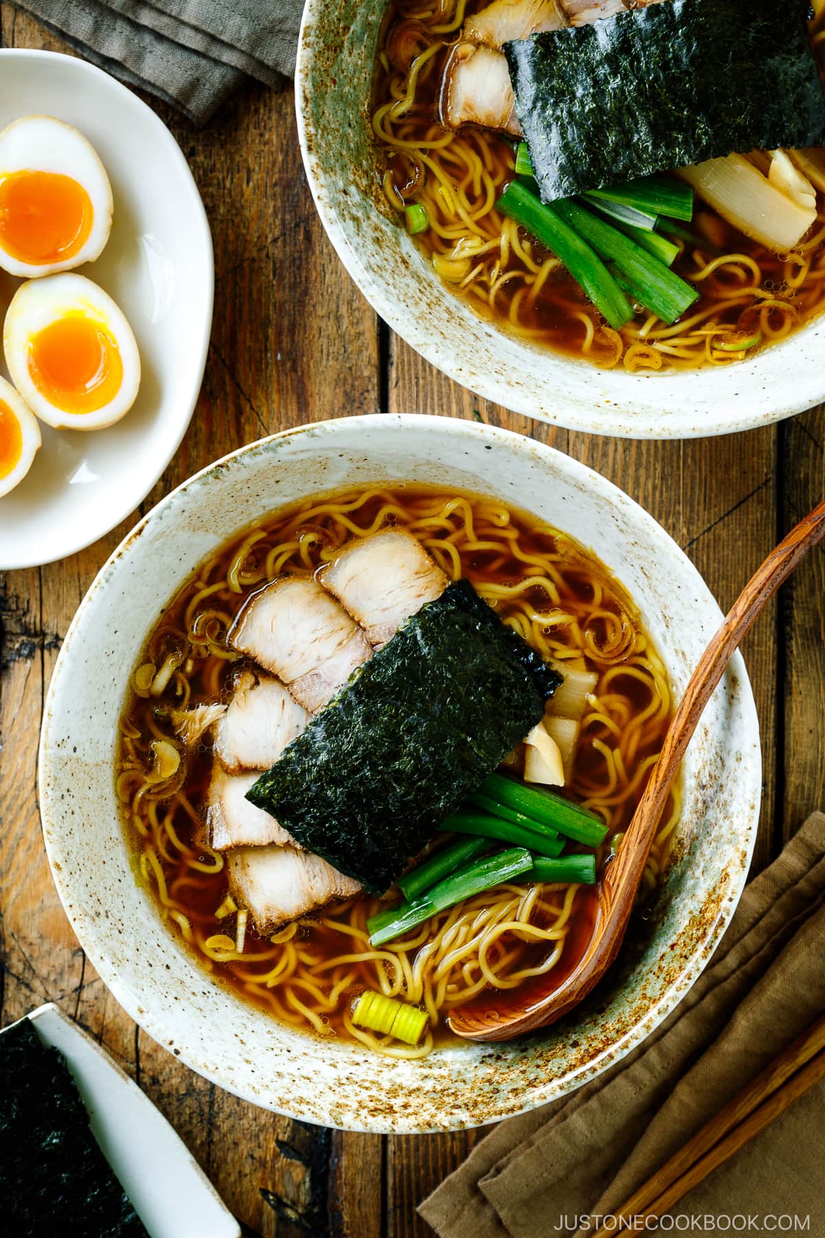 A ramen bowl containing shoyu ramen topped with chashu, seasoned bamboo shoots, green onion, and nori.