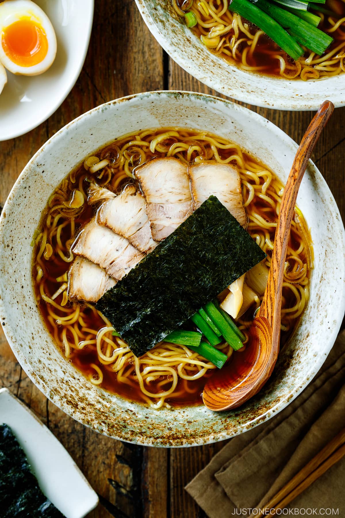 A ramen bowl containing shoyu ramen topped with chashu, seasoned bamboo shoots, green onion, and nori.