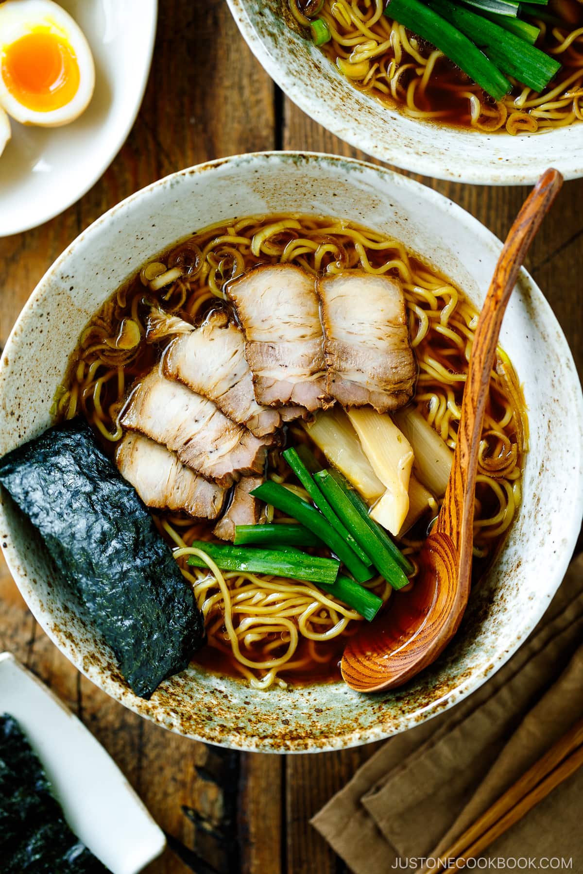 A ramen bowl containing shoyu ramen topped with chashu, seasoned bamboo shoots, green onion, and nori.