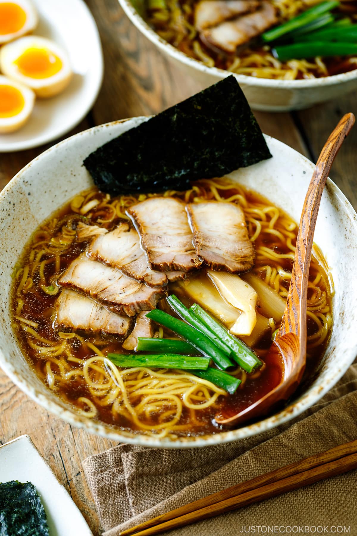 A ramen bowl containing shoyu ramen topped with chashu, seasoned bamboo shoots, green onion, and nori.