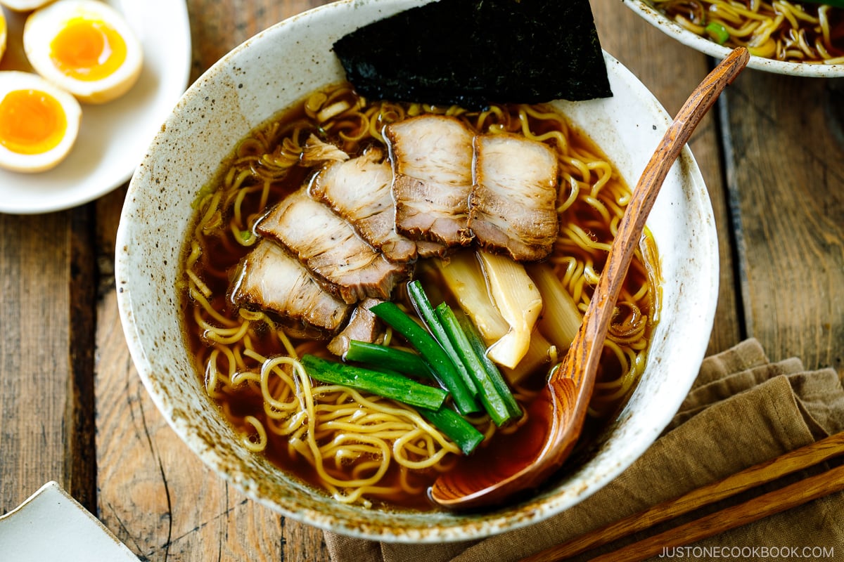 A ramen bowl containing shoyu ramen topped with chashu, seasoned bamboo shoots, green onion, and nori.