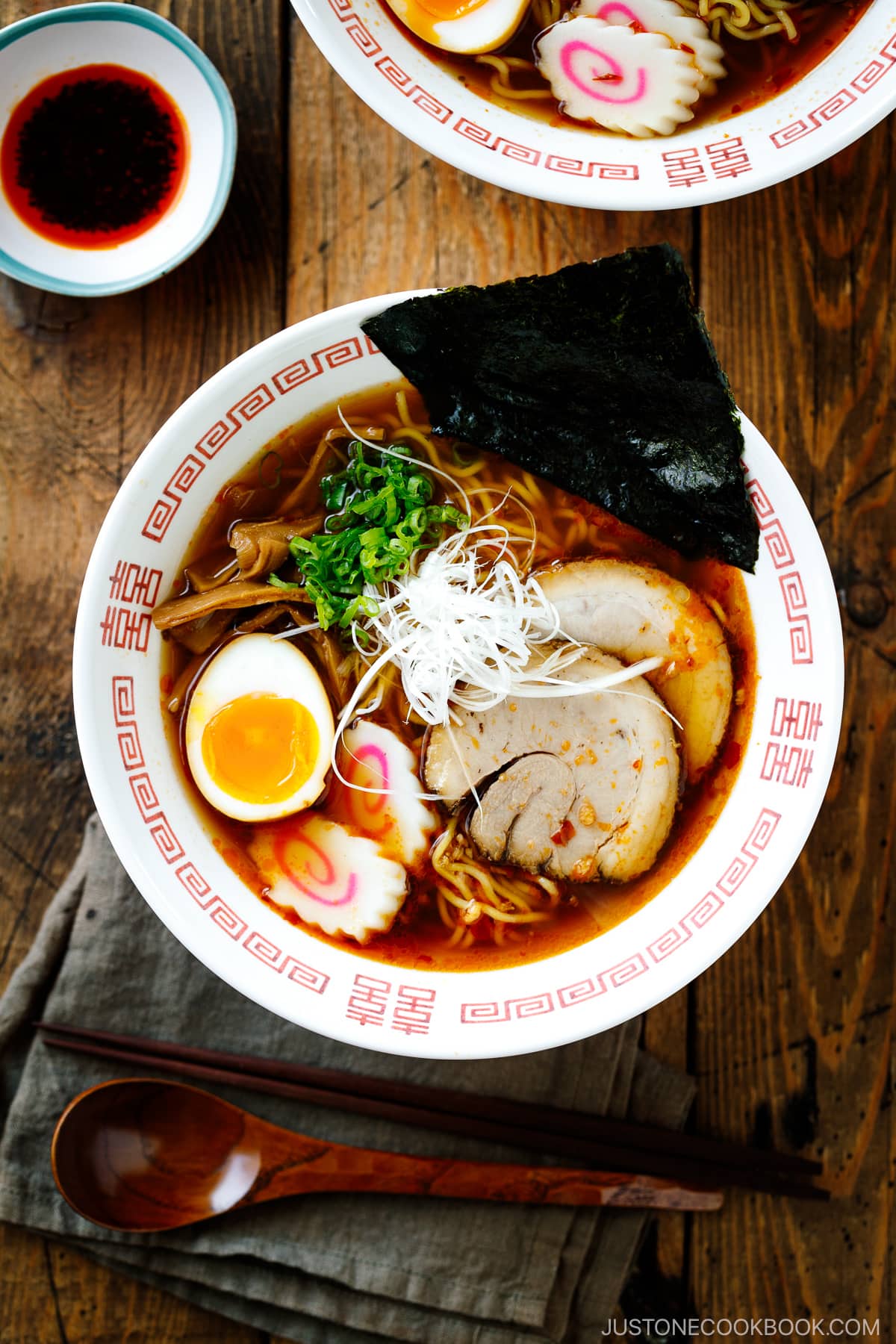 Ramen bowls containing Spicy Shoyu Ramen topped with chashu, marinated egg (ajitama), fish cake, scallions, and nori.