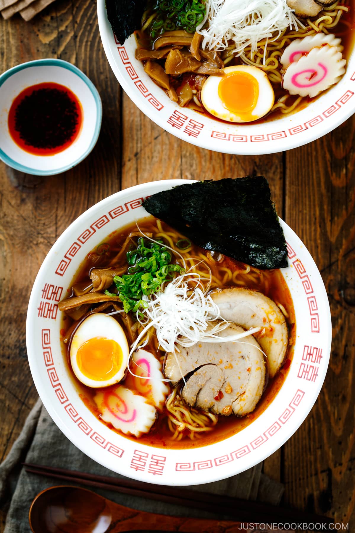 Ramen bowls containing Spicy Shoyu Ramen topped with chashu, marinated egg (ajitama), fish cake, scallions, and nori.