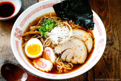 Ramen bowls containing Spicy Shoyu Ramen topped with chashu, marinated egg (ajitama), fish cake, scallions, and nori.