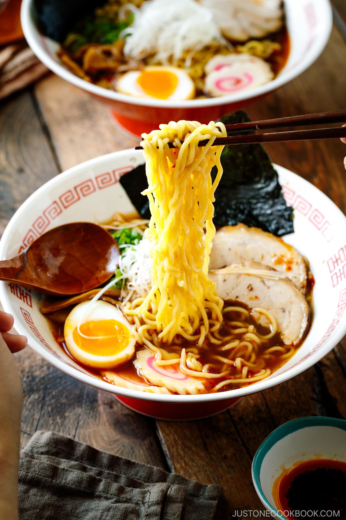 Ramen bowls containing Spicy Shoyu Ramen topped with chashu, marinated egg (ajitama), fish cake, scallions, and nori.