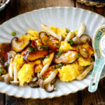 A fluted oval shape containing stir-fried mushrooms and eggs drizzled with ankake sauce.