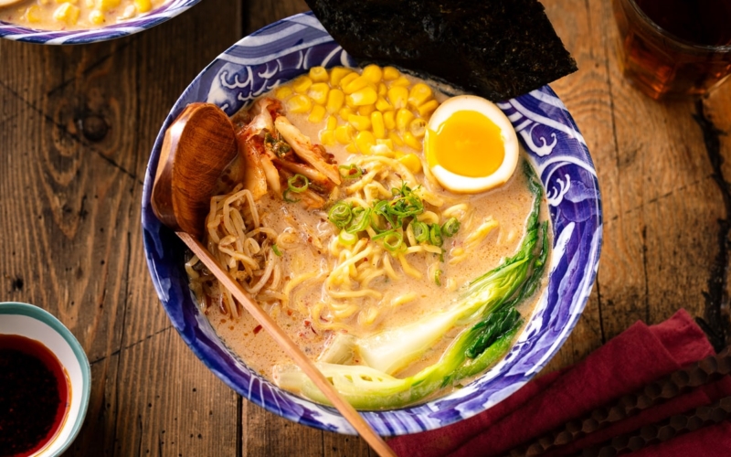 A bowl of Vegetarian Ramen topped with ajitama (soy marinated egg), spicy bean sprouts, corn, and a green veggie.