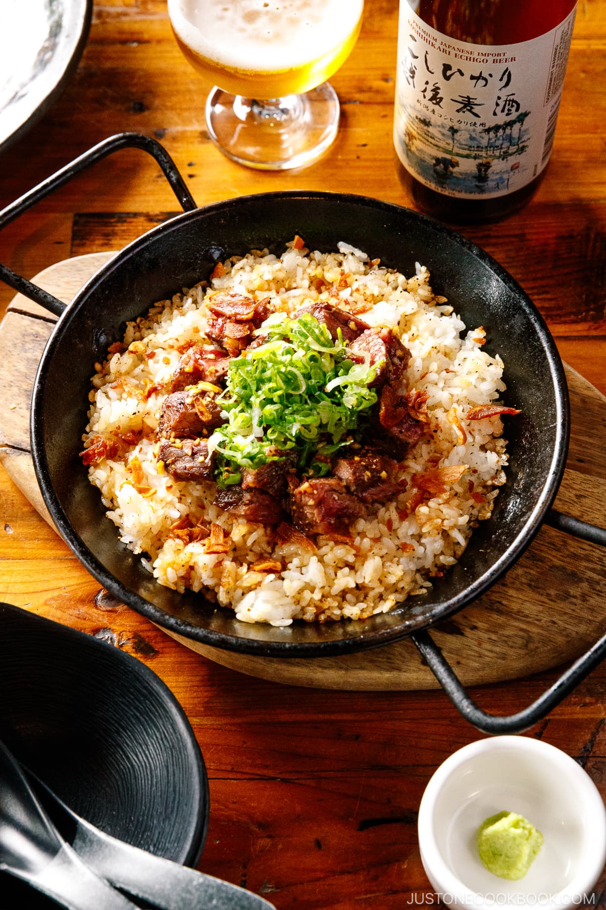 A paella pan containing Steak Garlic Rice topped with chopped scallions and garlic chips.