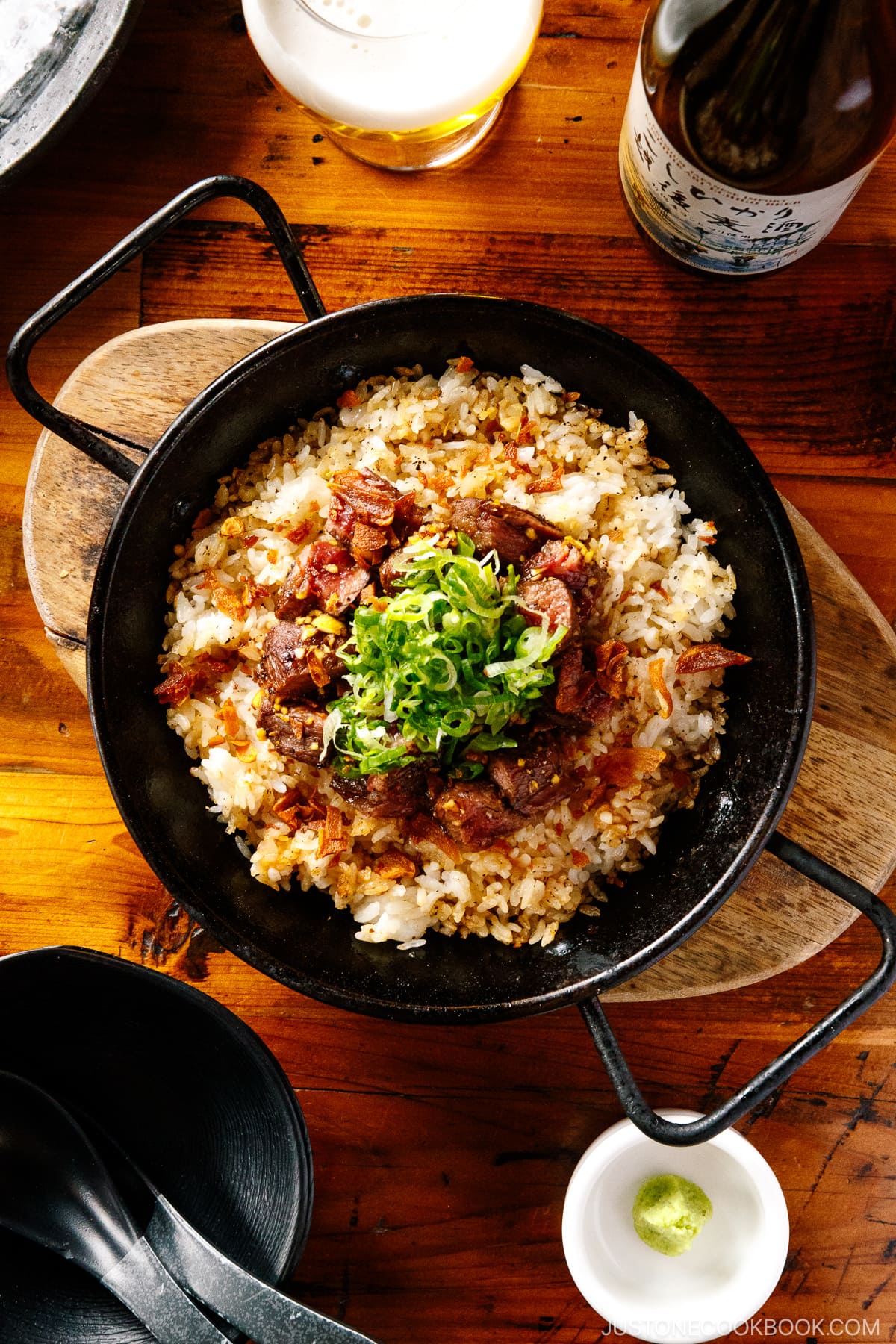 A paella pan containing Steak Garlic Rice topped with chopped scallions and garlic chips.