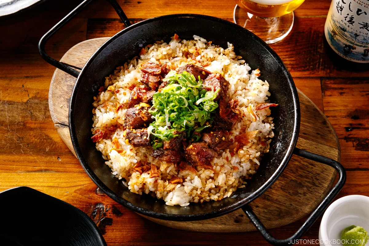 A paella pan containing Steak Garlic Rice topped with chopped scallions and garlic chips.