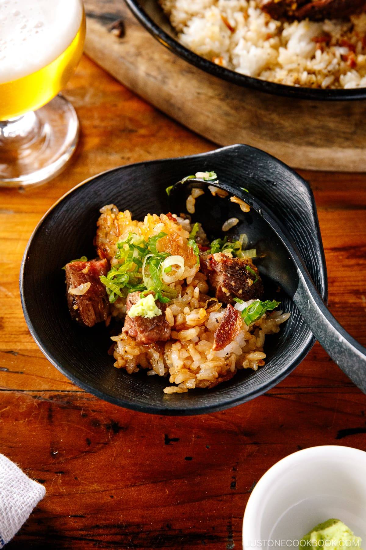 A black bowl containing Steak Garlic Rice topped with chopped scallions and garlic chips.