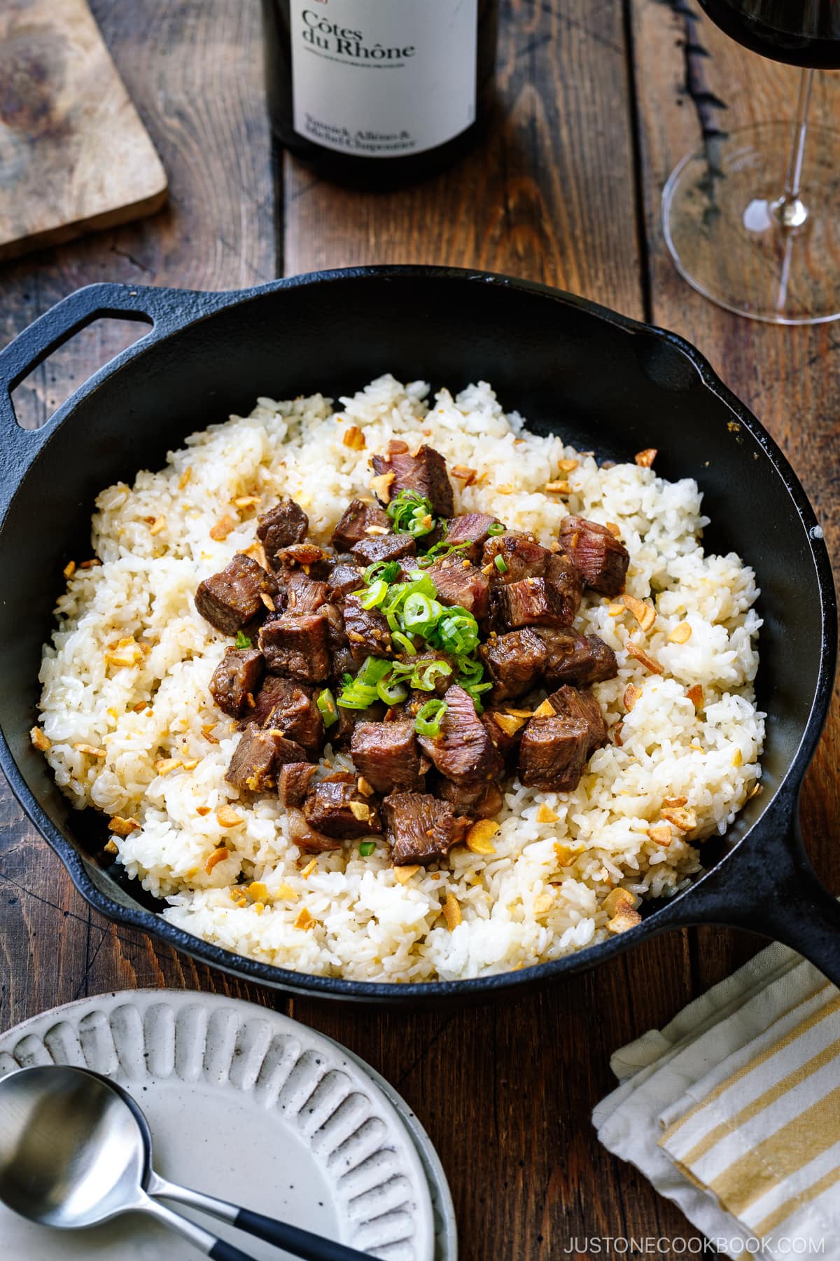A cast-iron pan containing Steak Garlic Rice topped with chopped scallions and garlic chips.