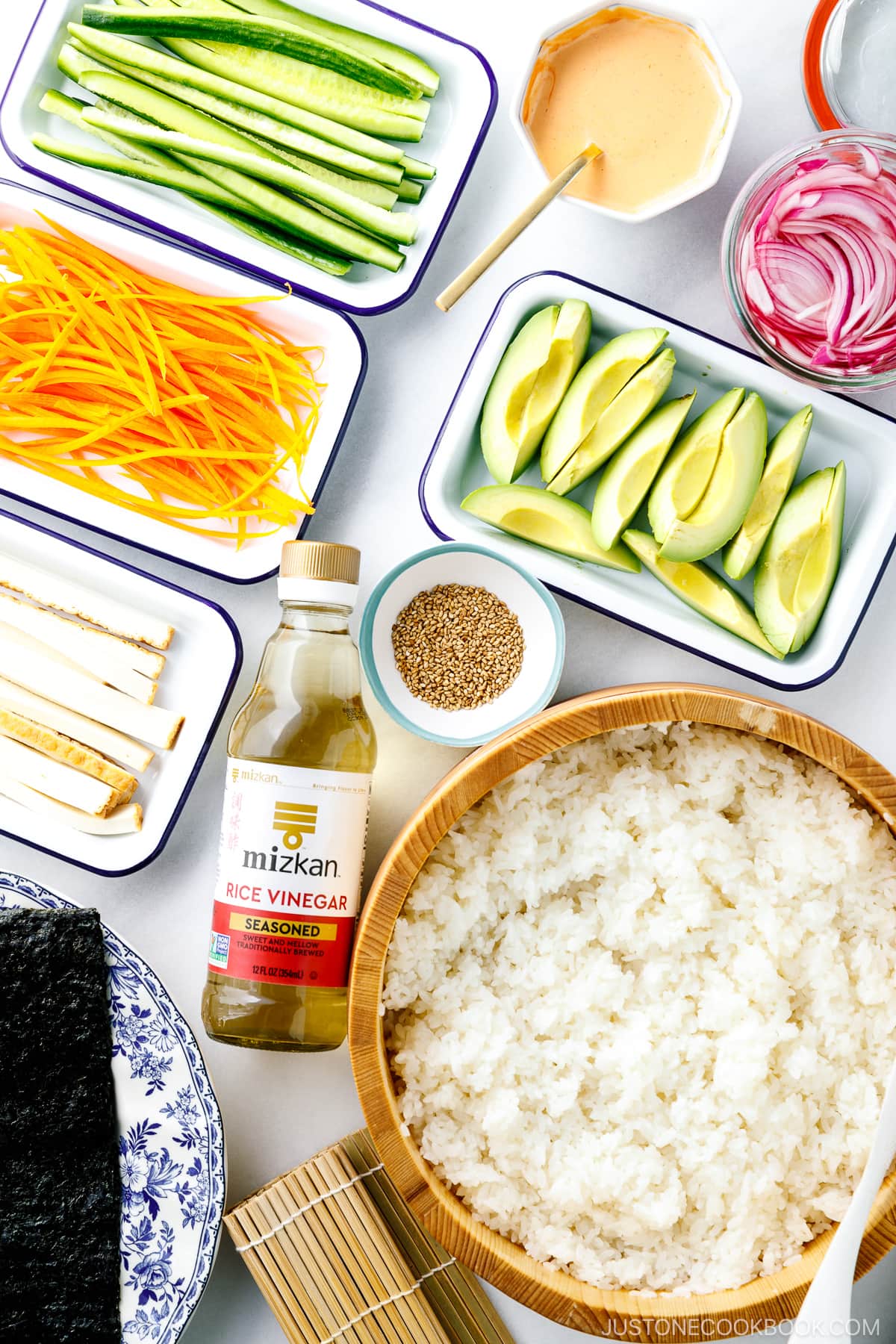 A wooden sushi oke container with sushi rice and prep trays filled with ingredients for vegetarian sushi rolls.