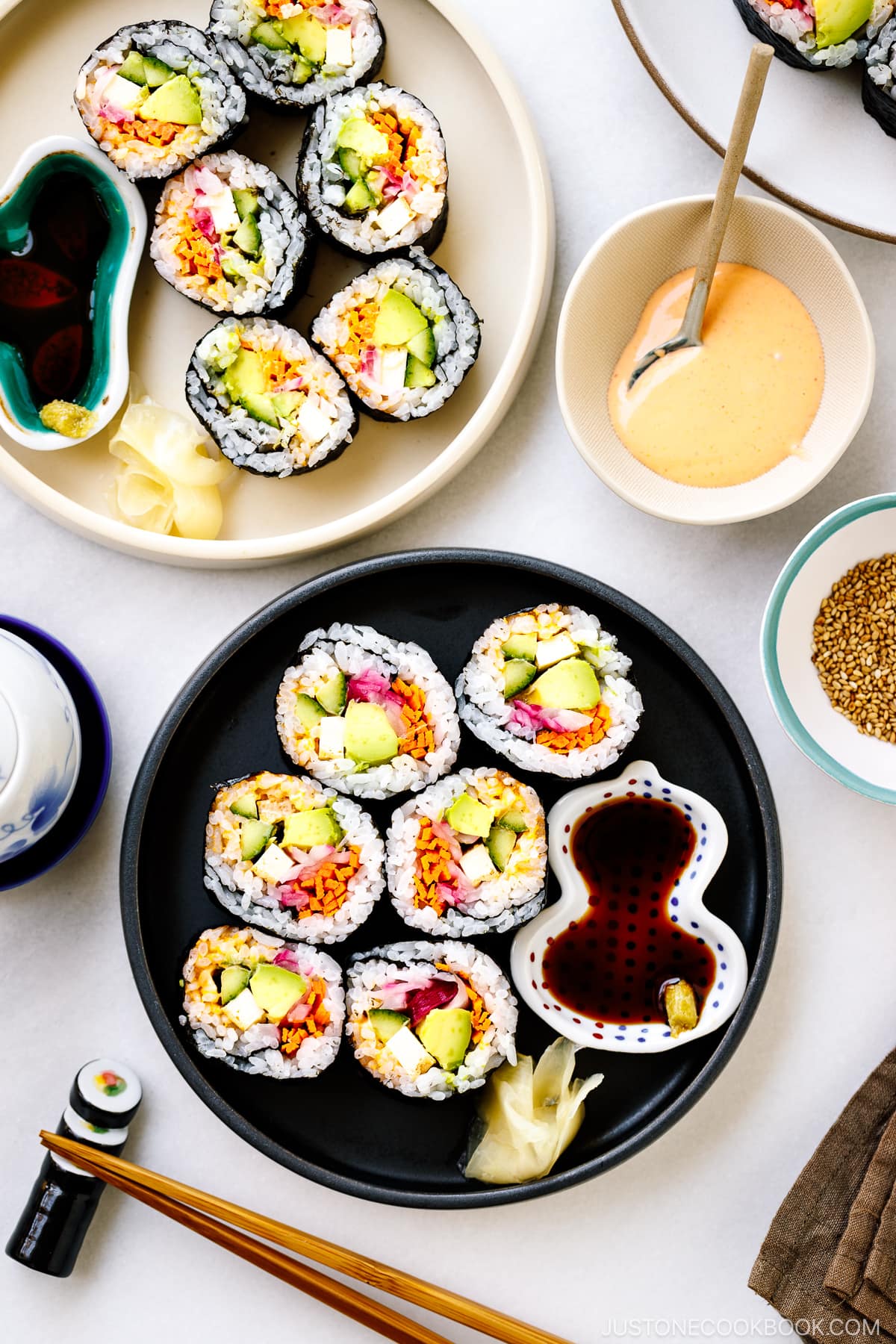 Black and white round plates containing colorful vegetarian sushi rolls.