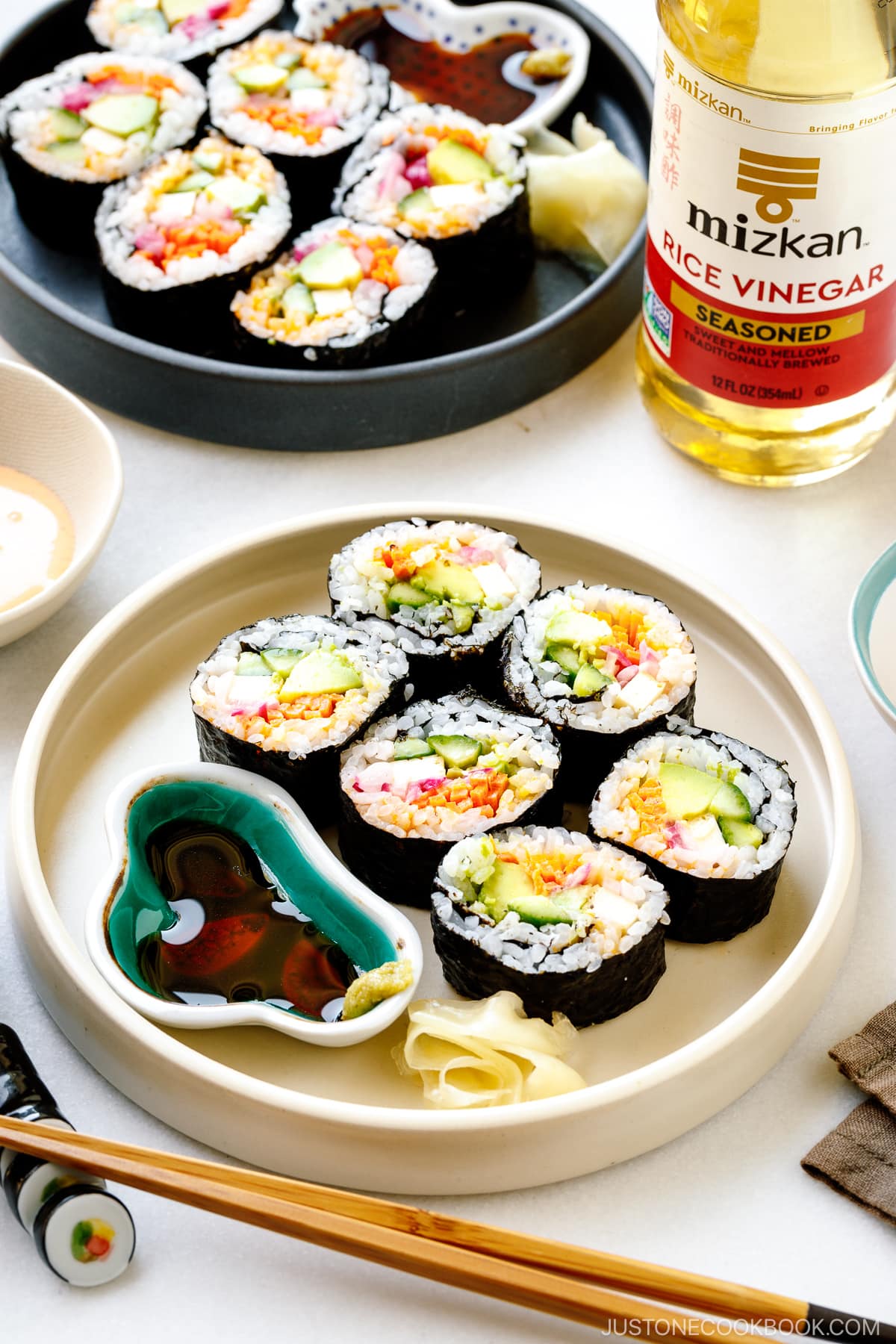 Black and white round plates containing colorful vegetarian sushi rolls.