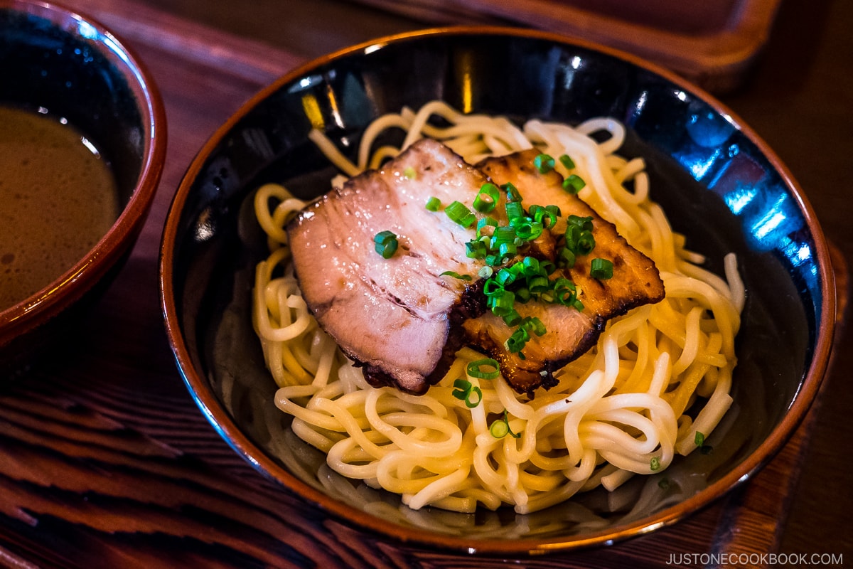 a bowl of dry noodle with pork slices on top