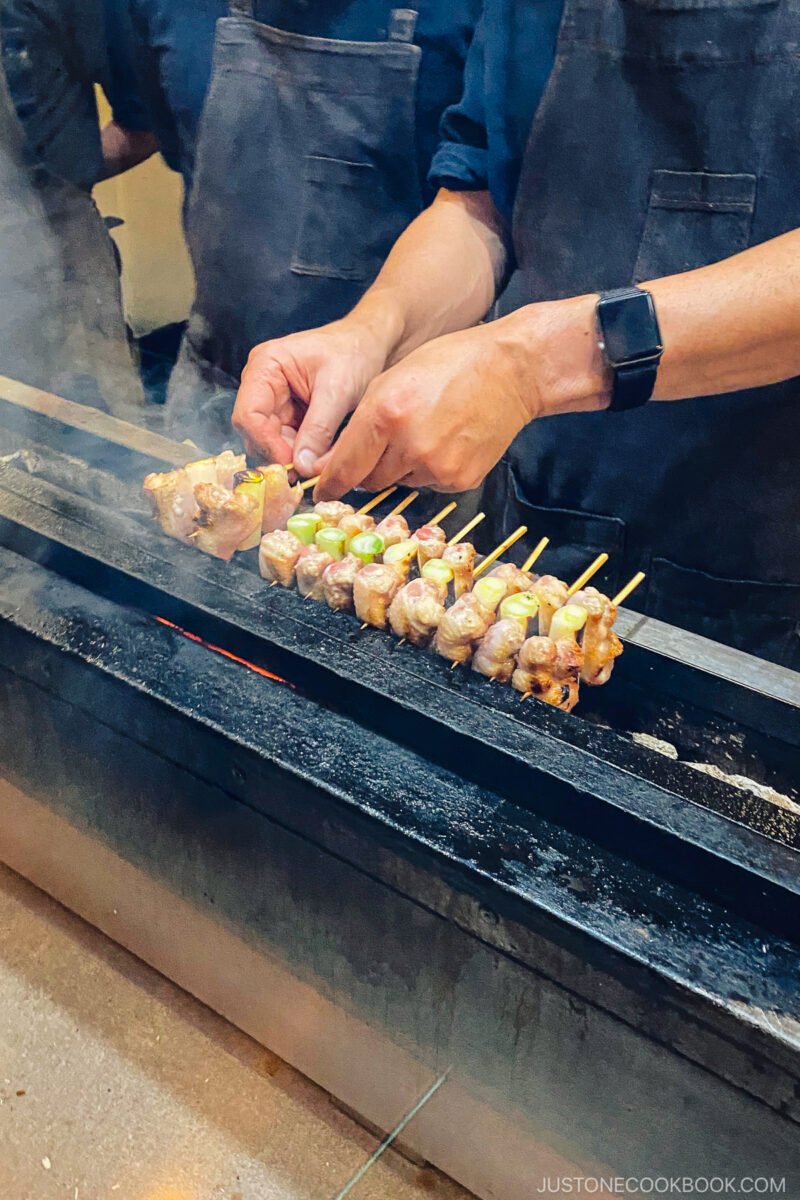 someone grilling skewers on top of charcoal