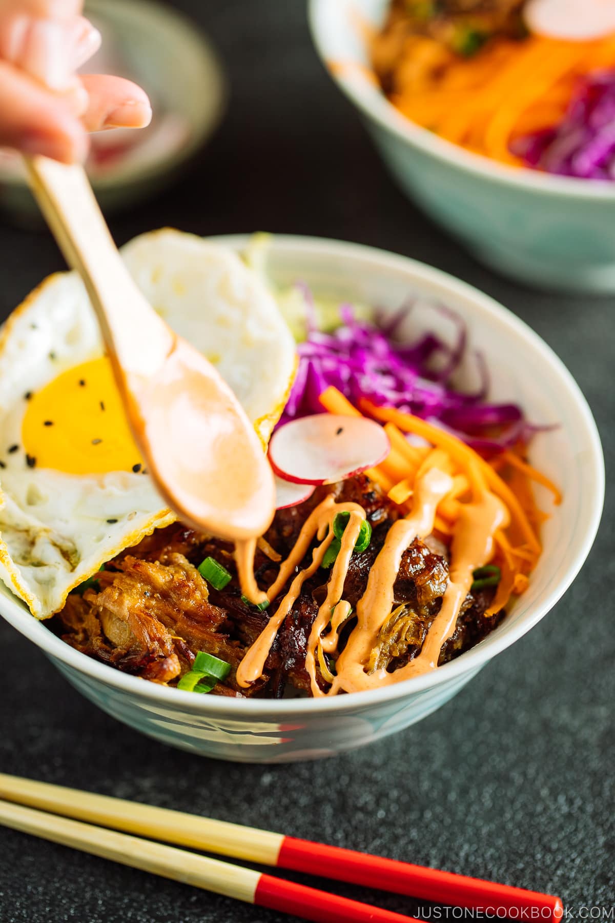 Plates and bowls containing ingredients for Asian Pulled Pork Bowls, including steamed rice, fried eggs, veggies, and spicy mayo.