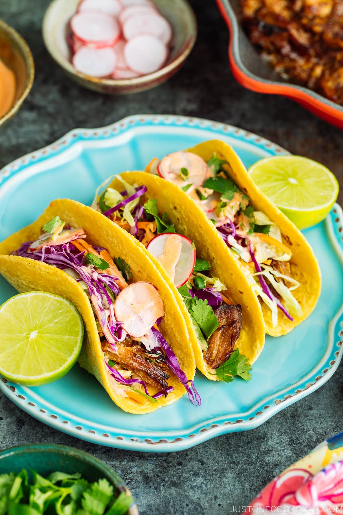 The wooden table with bowls and plates containing Asian Pulled Pork Taco ingredients.