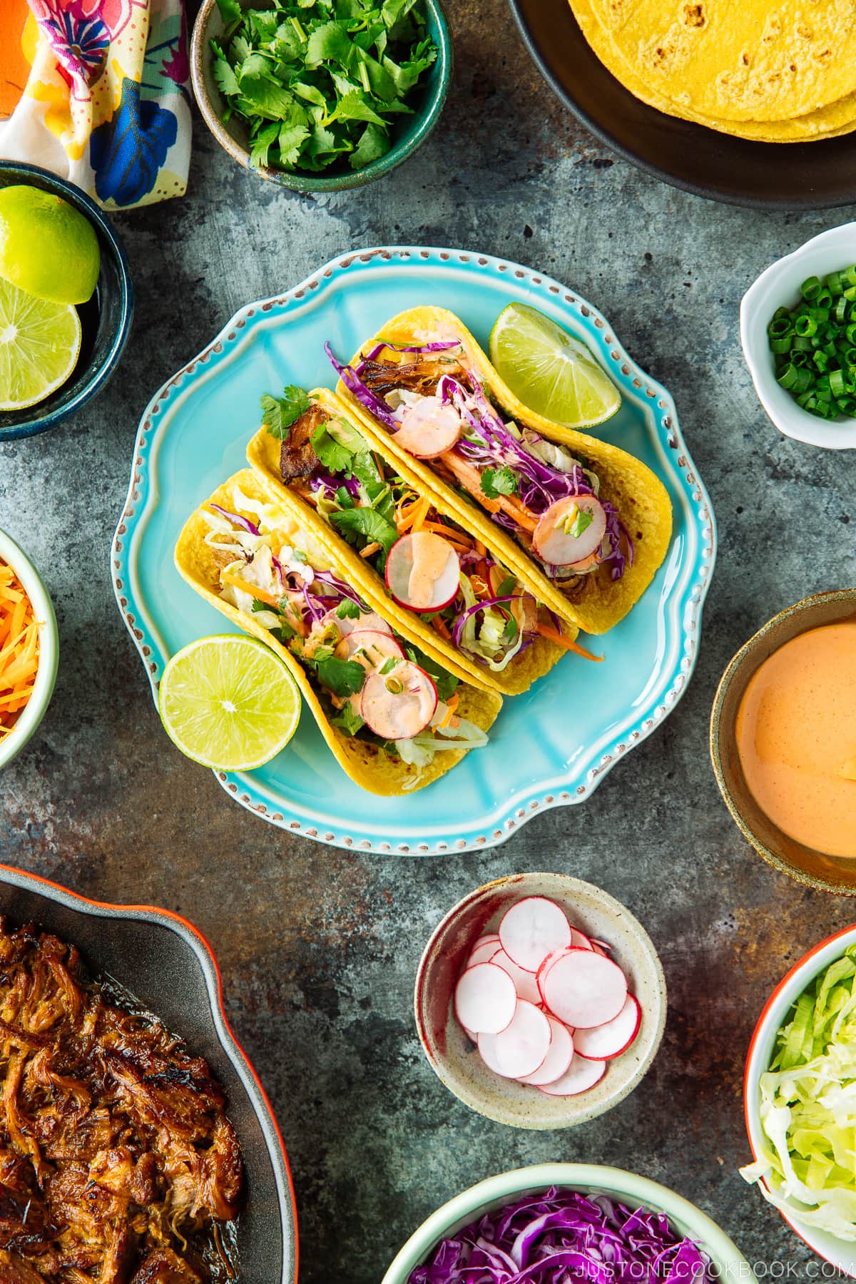 The wooden table with bowls and plates containing Asian Pulled Pork Taco ingredients.