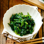 A white fluted dish containing Japanese spinach salad seasoned with sesame seeds, soy sauce, and sugar.