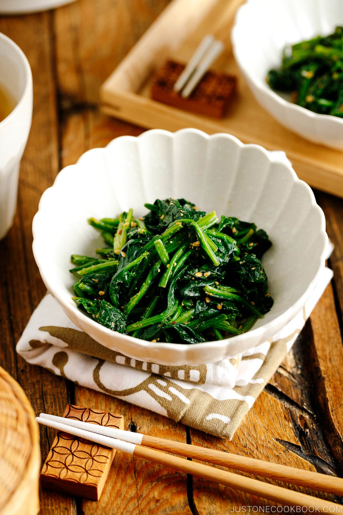 A white fluted dish containing Japanese spinach salad seasoned with sesame seeds, soy sauce, and sugar.