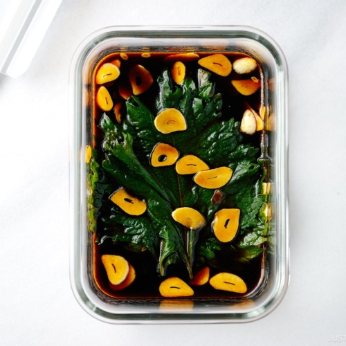 A glass container with fresh shiso leaves marinated in garlic soy sauce.