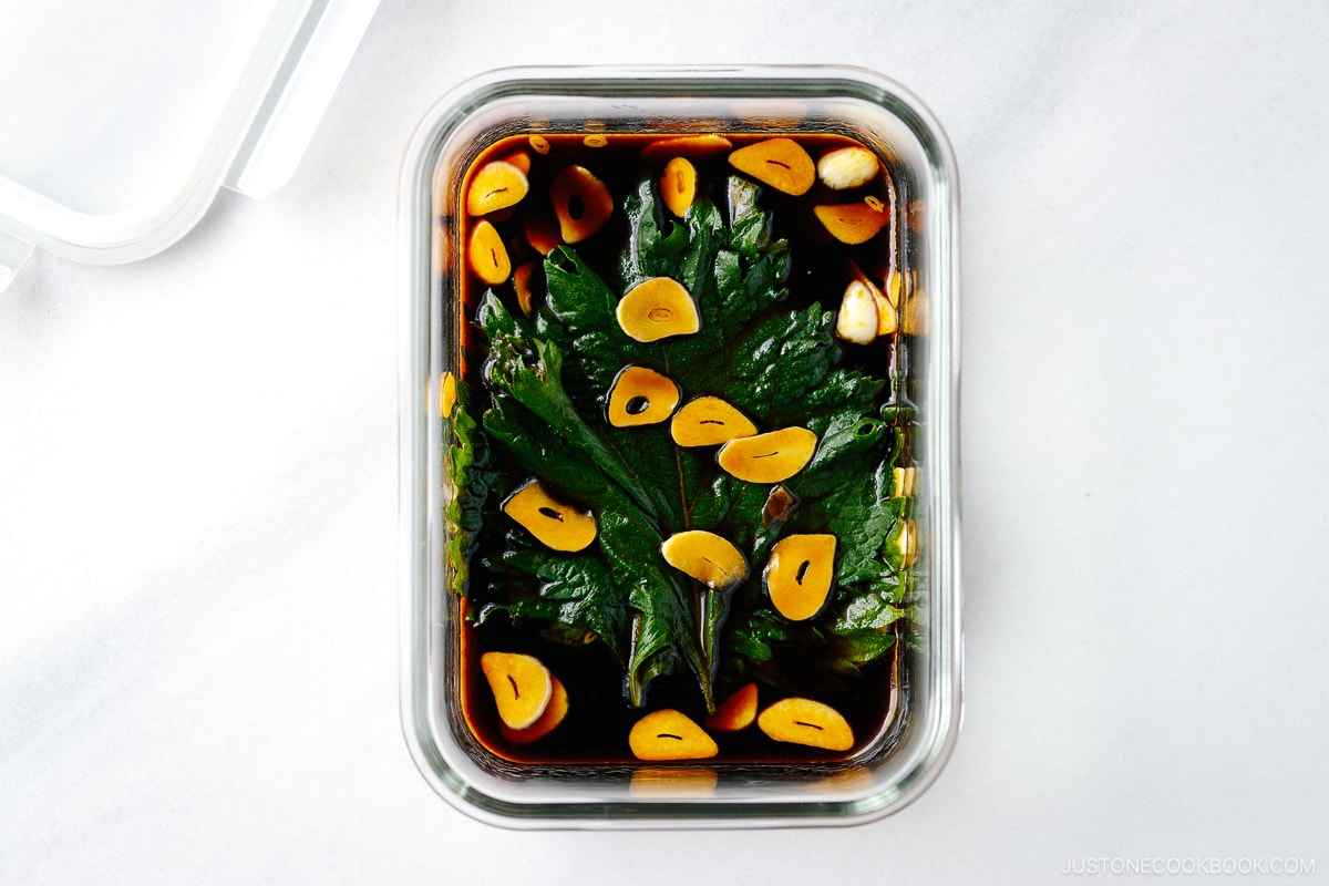 A glass container with fresh shiso leaves marinated in garlic soy sauce.