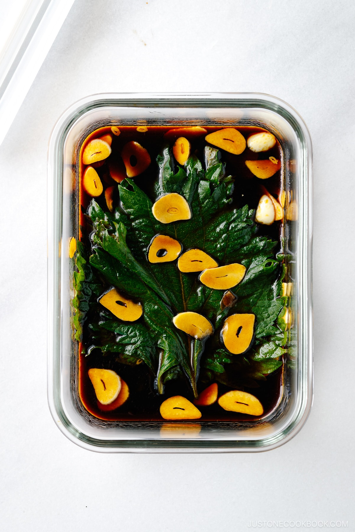 A glass container with fresh shiso leaves marinated in garlic soy sauce.