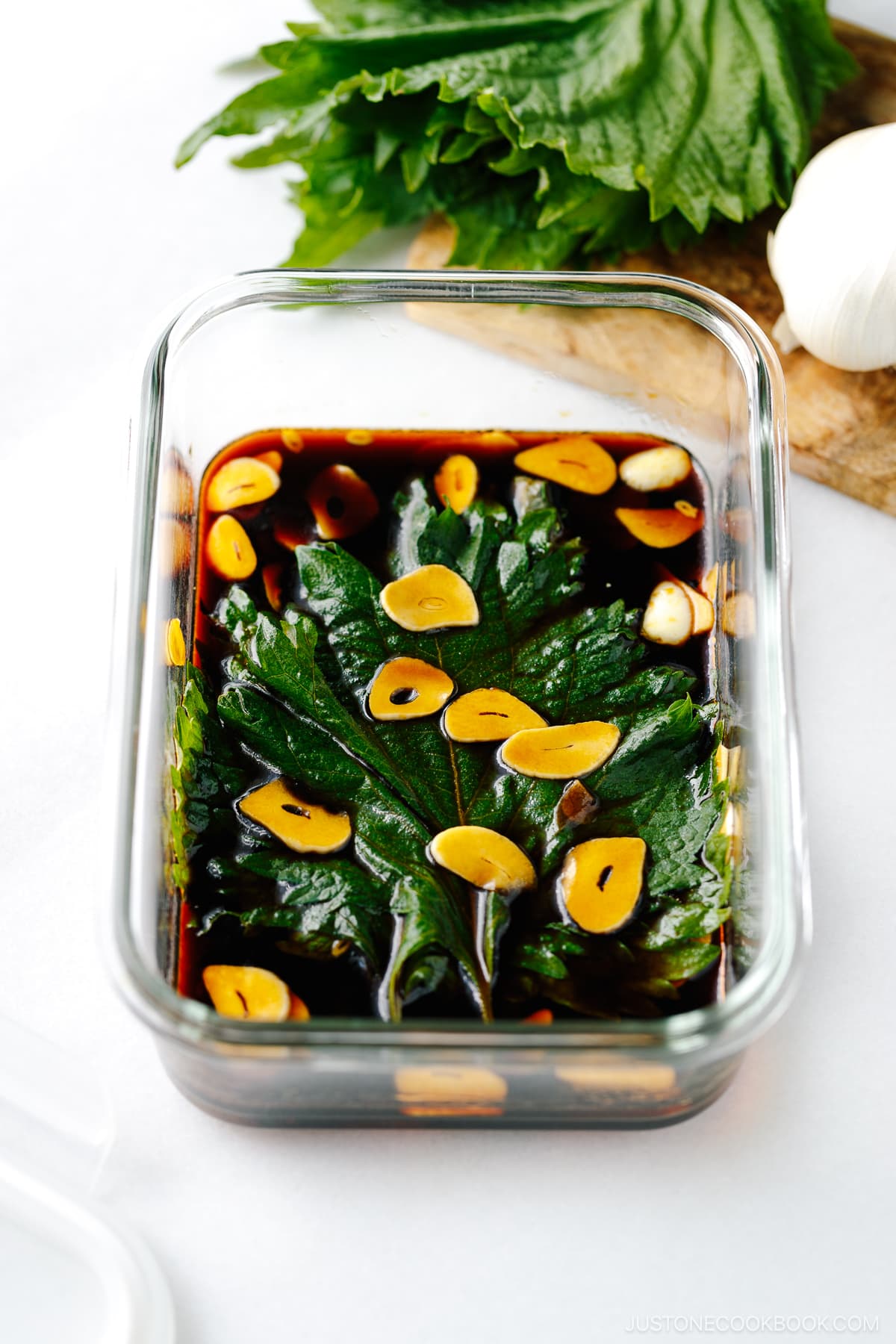 A glass container with fresh shiso leaves marinated in garlic soy sauce.