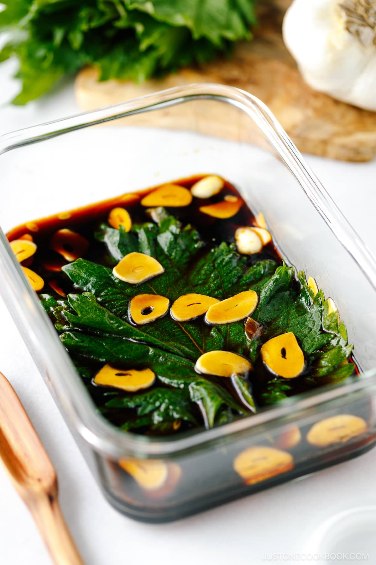 A glass container with fresh shiso leaves marinated in garlic soy sauce.