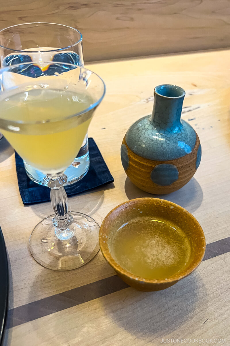 sake in a cup next to tall glasses