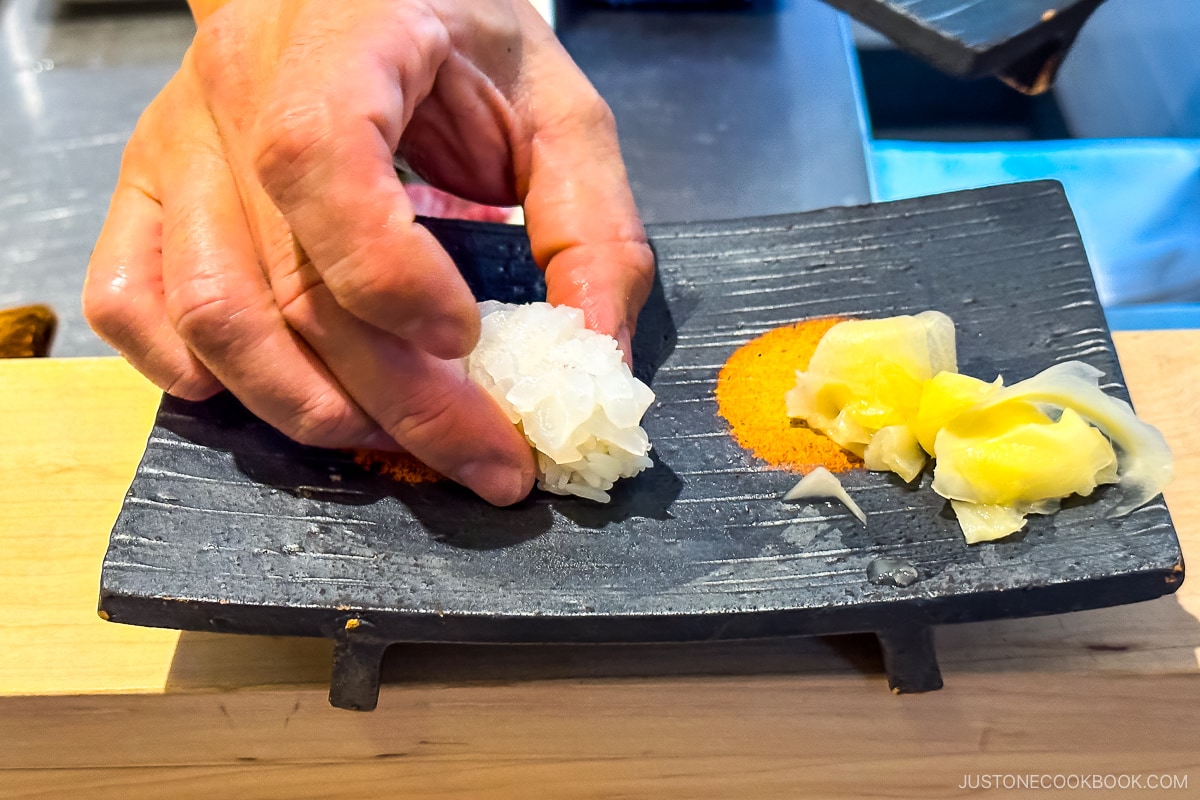 squid sushi being served on a black plate