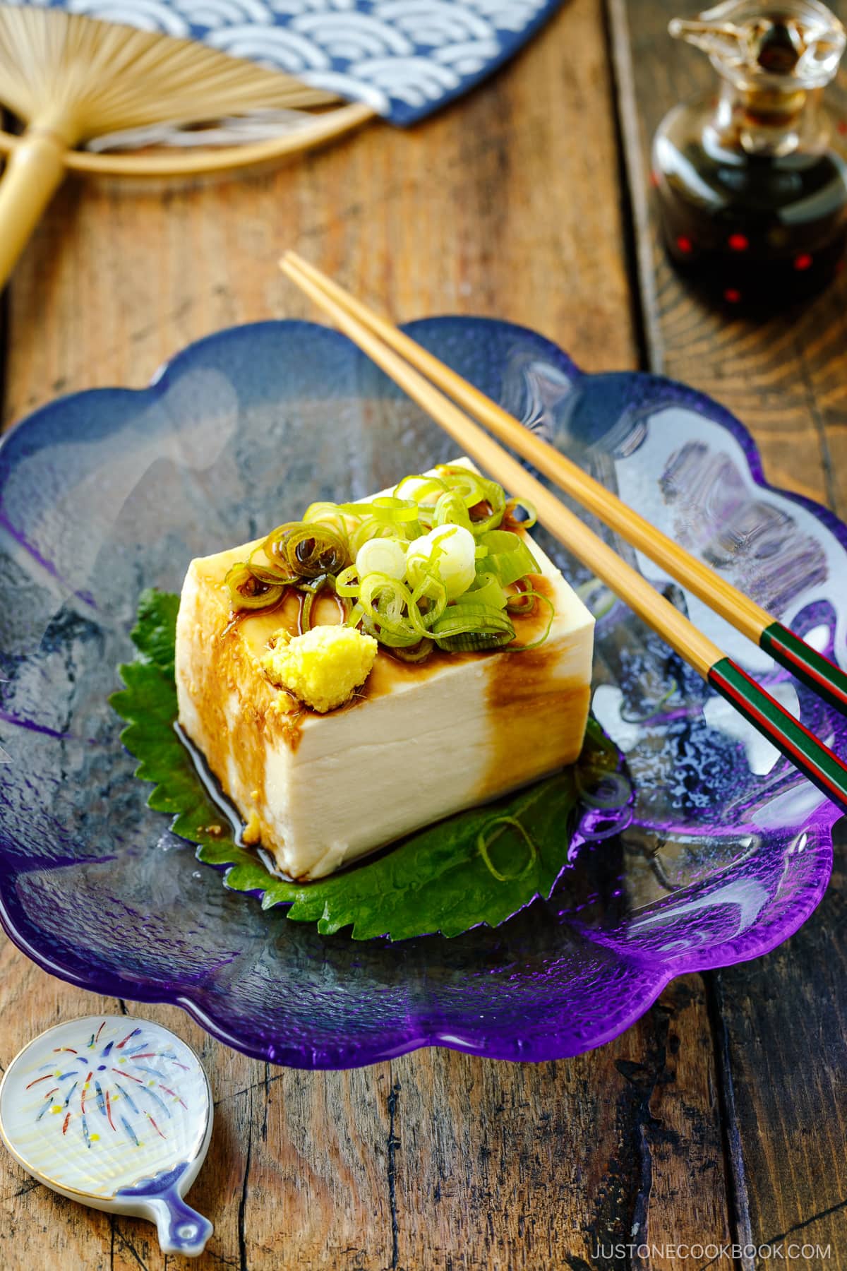 A glassware containing Japanese cold tofu topped with green onion and grated ginger and drizzled with soy sauce.