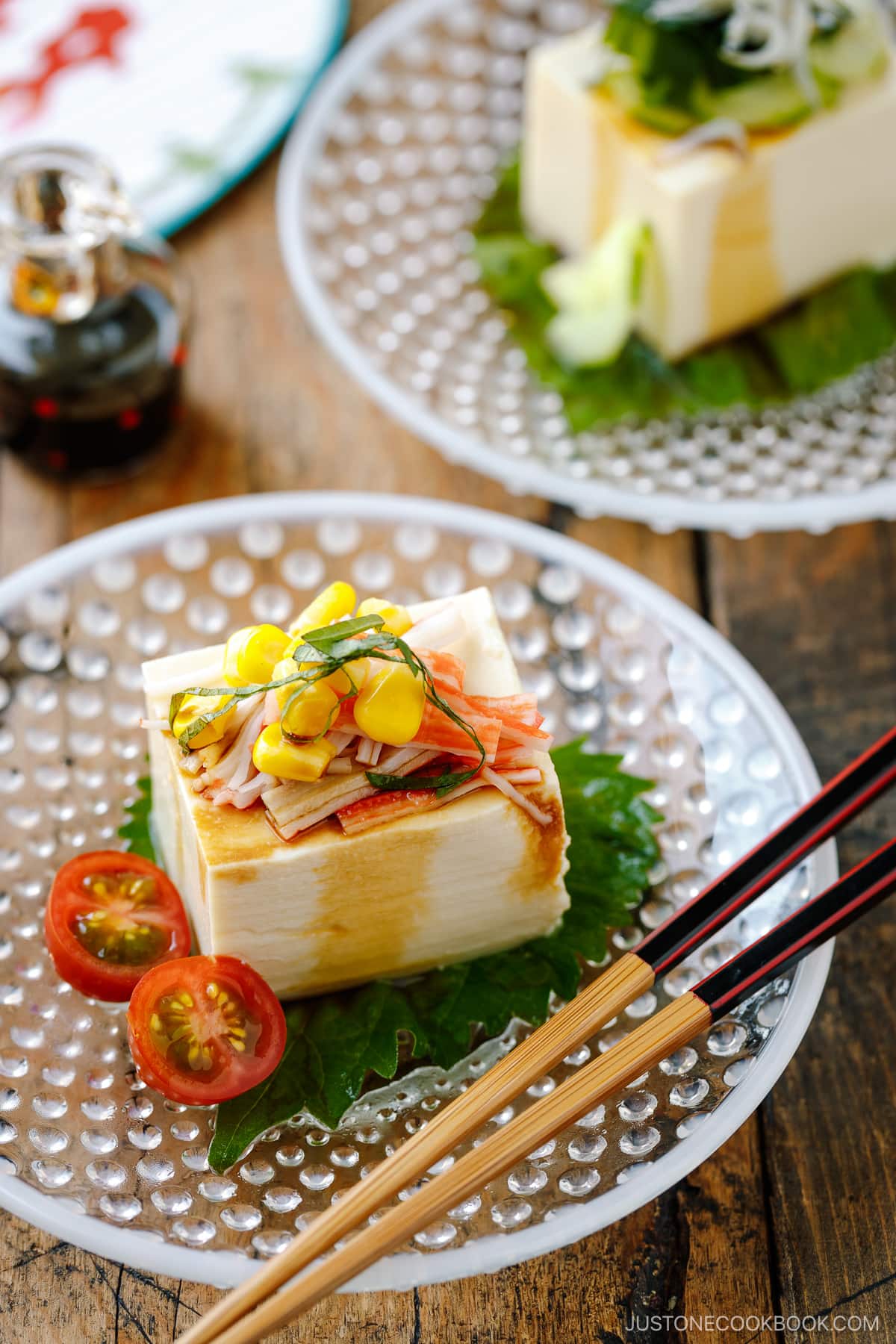 A glassware containing Japanese cold tofu topped with crabmeat, corn, and julienned shiso and drizzled with soy sauce.