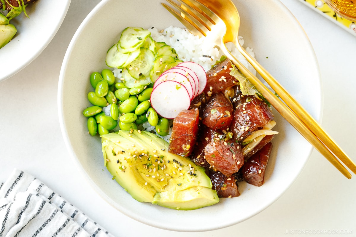 Ahi Tuna Poke Bowl containing soy marinated raw tuna, avocado slices, edamame, and cucumber slices over a bed of steamed rice.