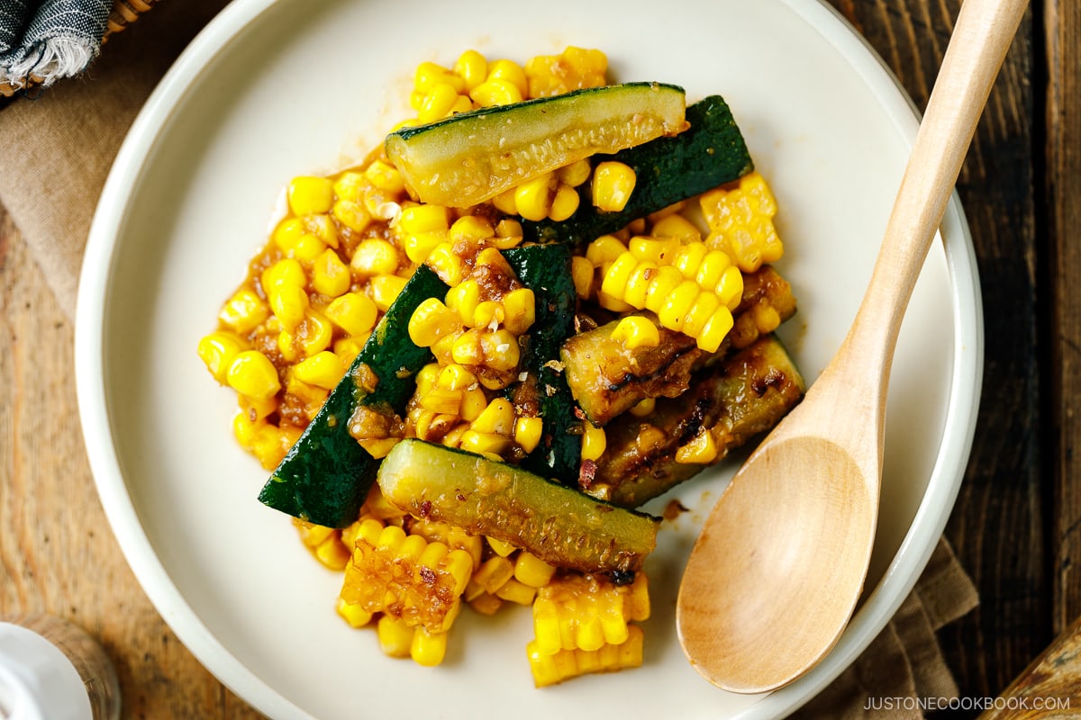 A white plate containing zucchini corn stir fry seasoned with miso butter.