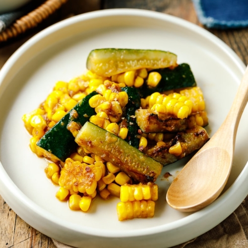 A white plate containing zucchini corn stir fry seasoned with miso butter.