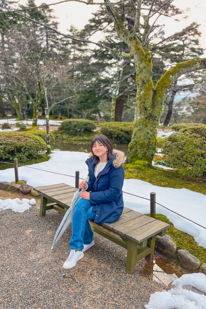 a girl sitting on a bench in front of snow covered grounds