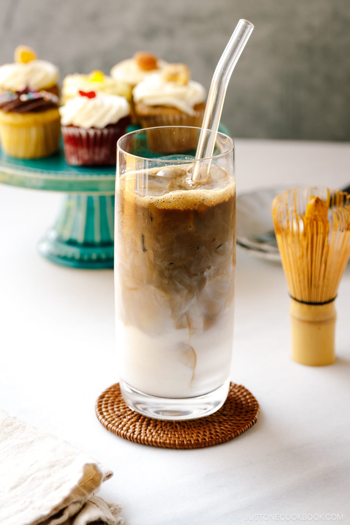 A tall glass filled with iced hojicha latte, showing two layers of milk and chocolate-color roasted green tea (hojicha).