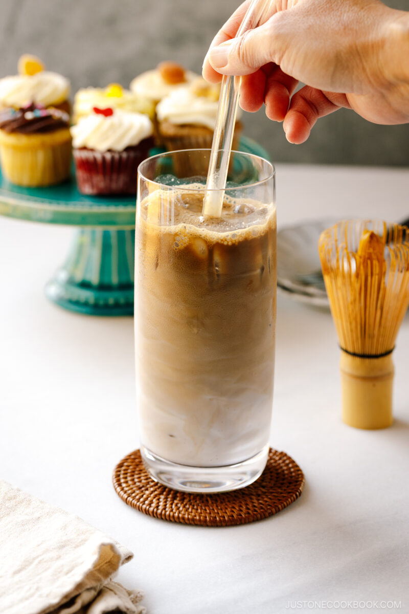 A tall glass filled with iced hojicha latte, showing two layers of milk and chocolate-color roasted green tea (hojicha).