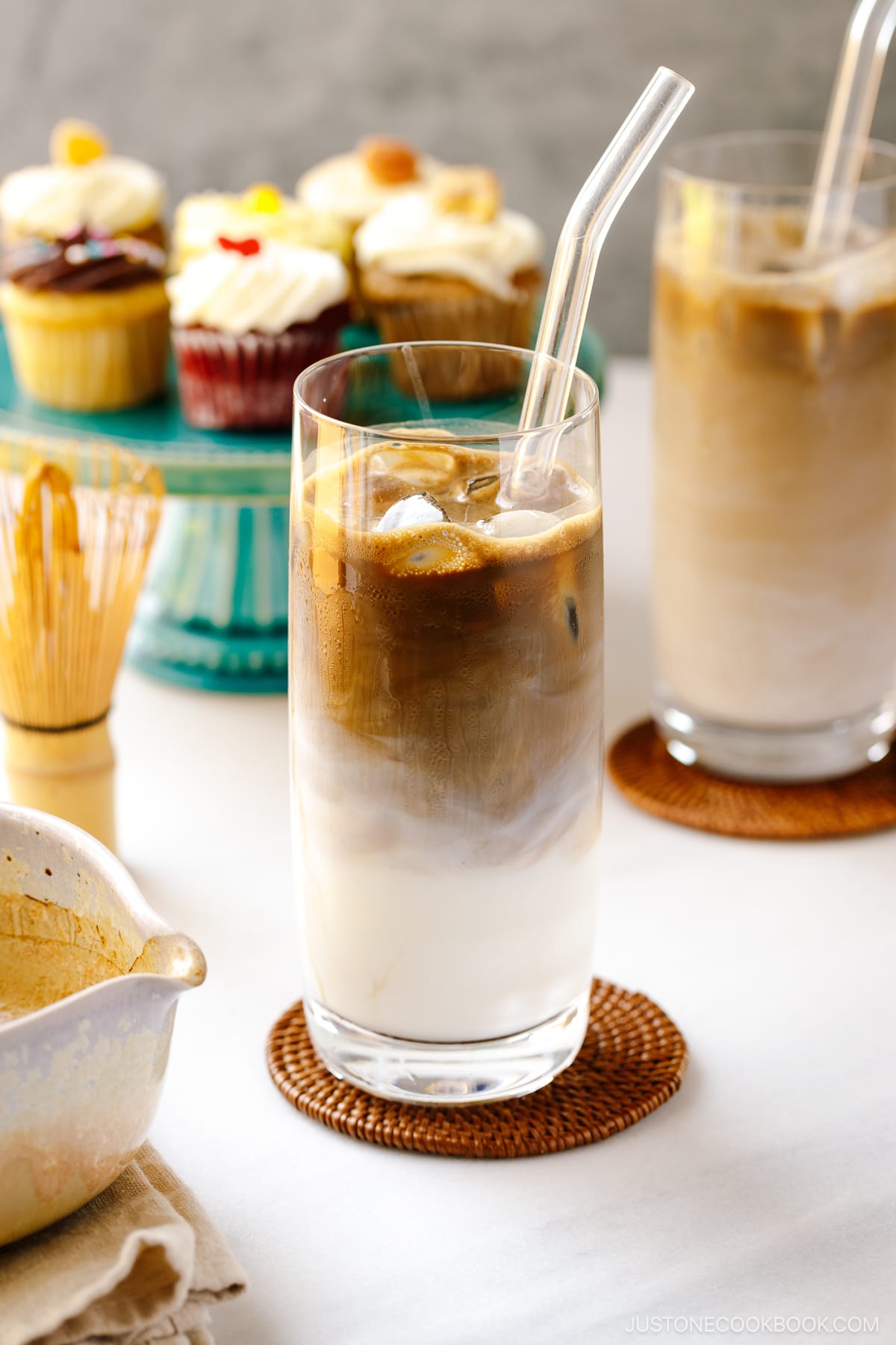 A tall glass filled with iced hojicha latte, showing two layers of milk and chocolate-color roasted green tea (hojicha).