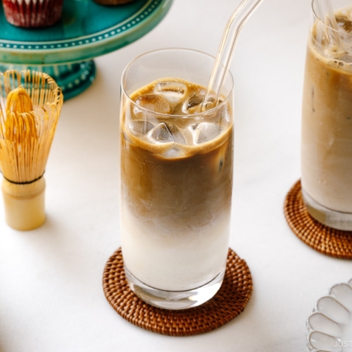 A tall glass filled with iced hojicha latte, showing two layers of milk and chocolate-color roasted green tea (hojicha).