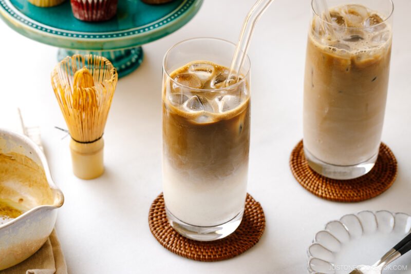 A tall glass filled with iced hojicha latte, showing two layers of milk and chocolate-color roasted green tea (hojicha).