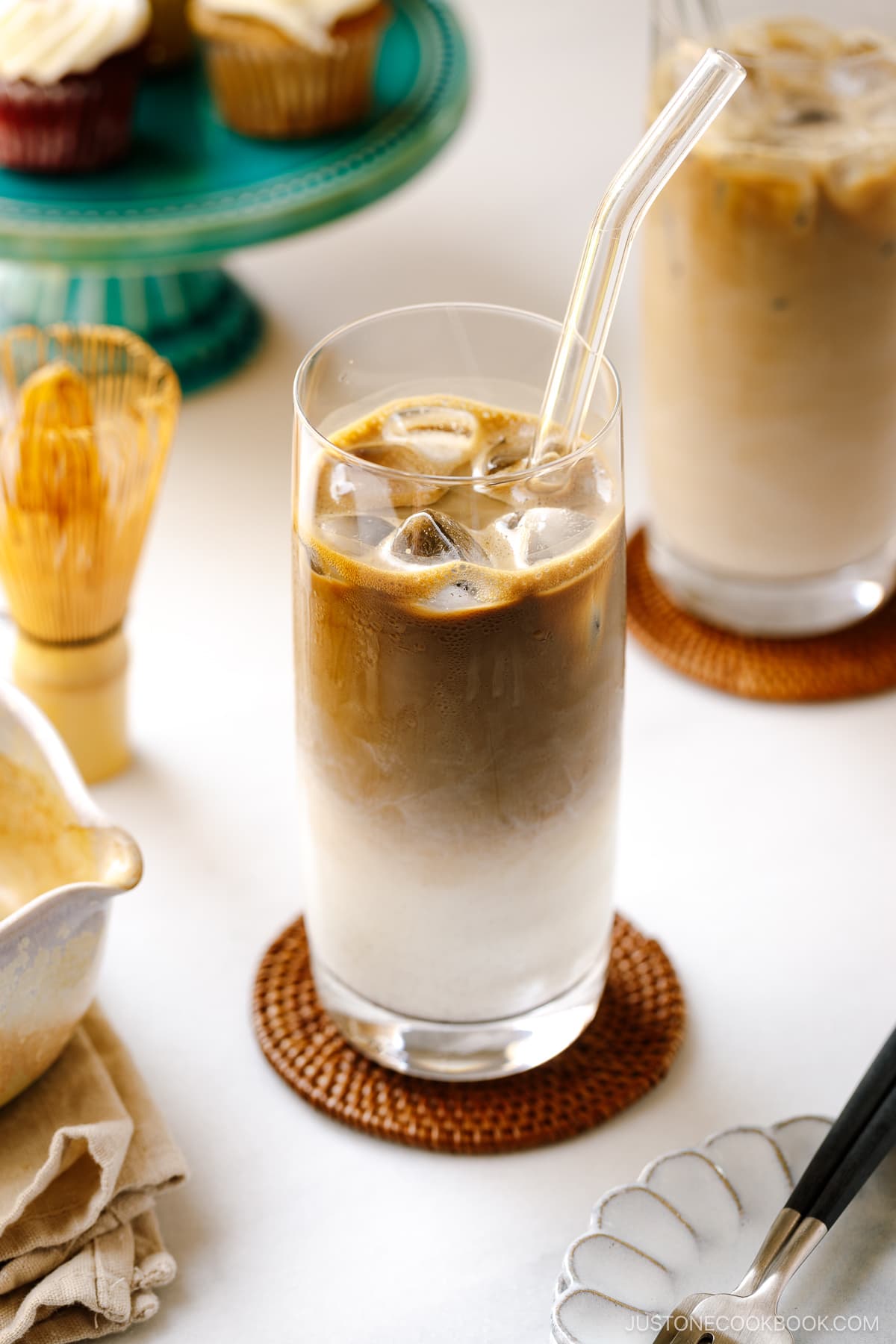 A tall glass filled with iced hojicha latte, showing two layers of milk and chocolate-color roasted green tea (hojicha).